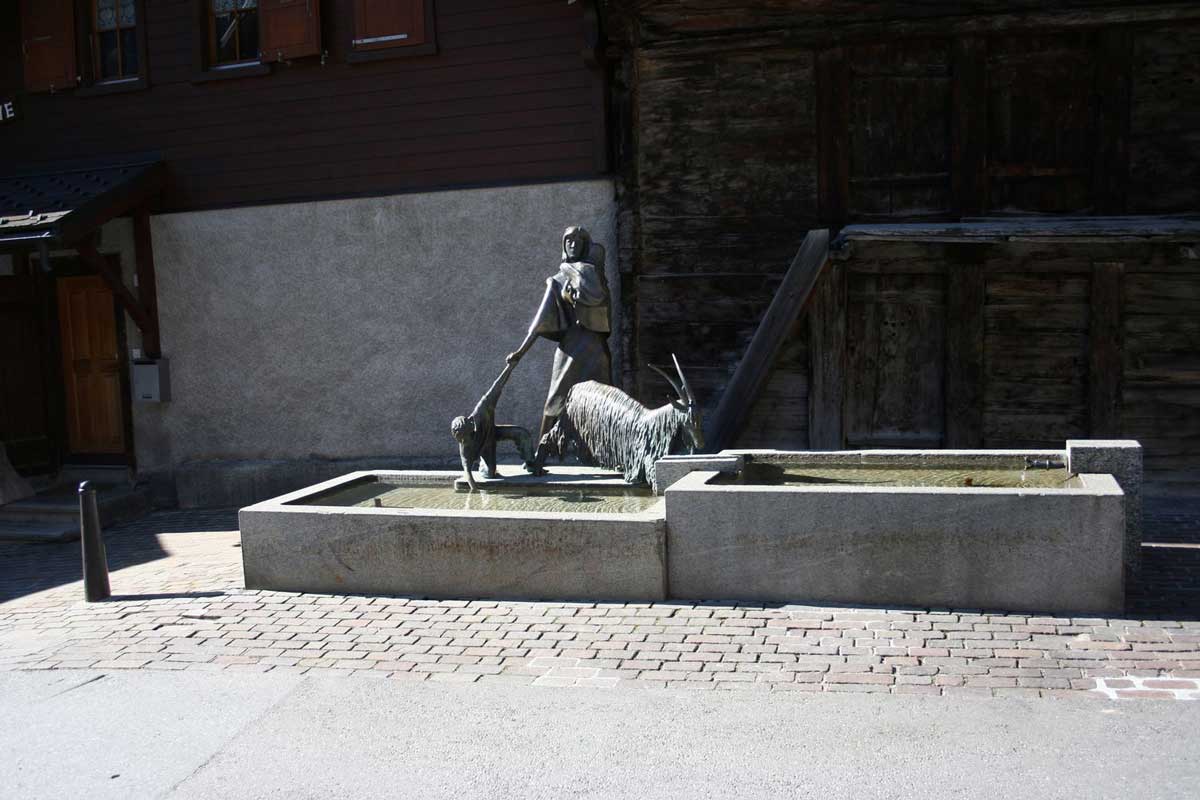 Fontaine en pierre avec une statue d'une femme avec son enfant et sa chèvre