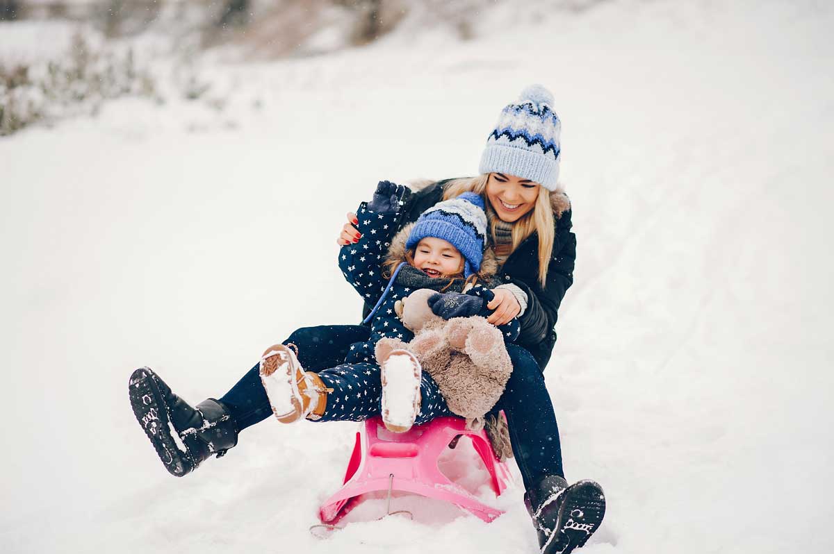 Petite fille avec sa mere jouant dans un parc d'hiver, en train de descendre une piste, sur une luge